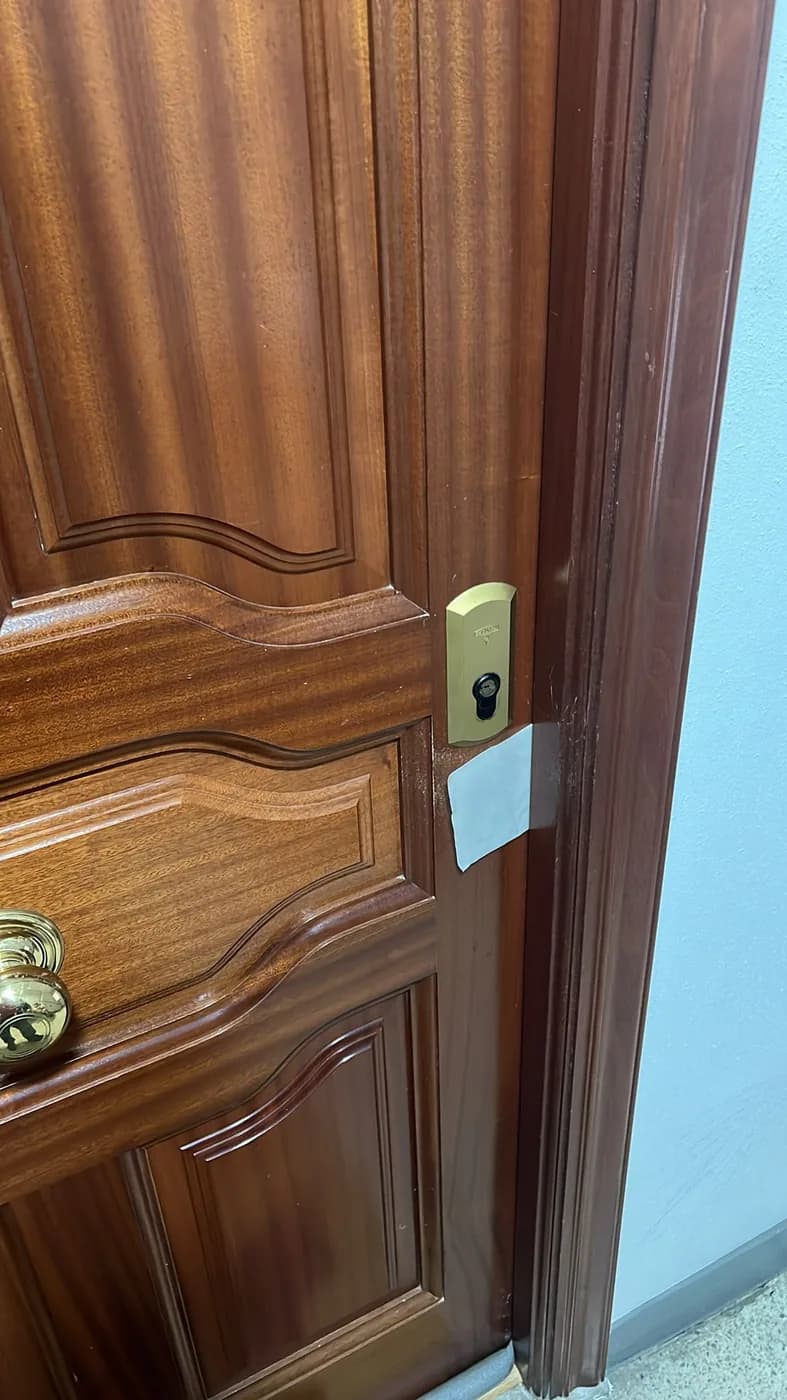 Cerradura de sobreponer dorada recién instalada en el canto de una puerta de piso de madera barnizada